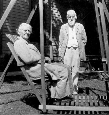 Mary seated in outdoor glider with C W standing nearby